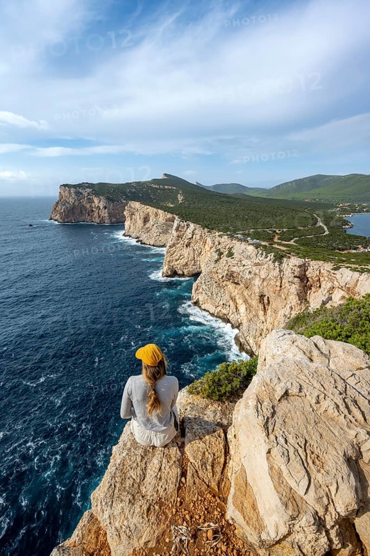 Tourist sitting on the edge of a steep cliff, view of steep cliffs by the sea, coastal landscape, cliffs on the Capo Caccia headland, Alghero, Sardinia, Italy