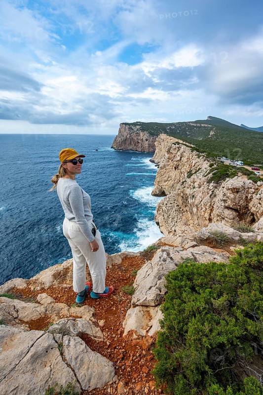 Tourist enjoying the view of steep cliffs by the sea and the rocky island of Isola Foradada, cliffs on the Capo Caccia headland, Alghero, Sardinia, Italy