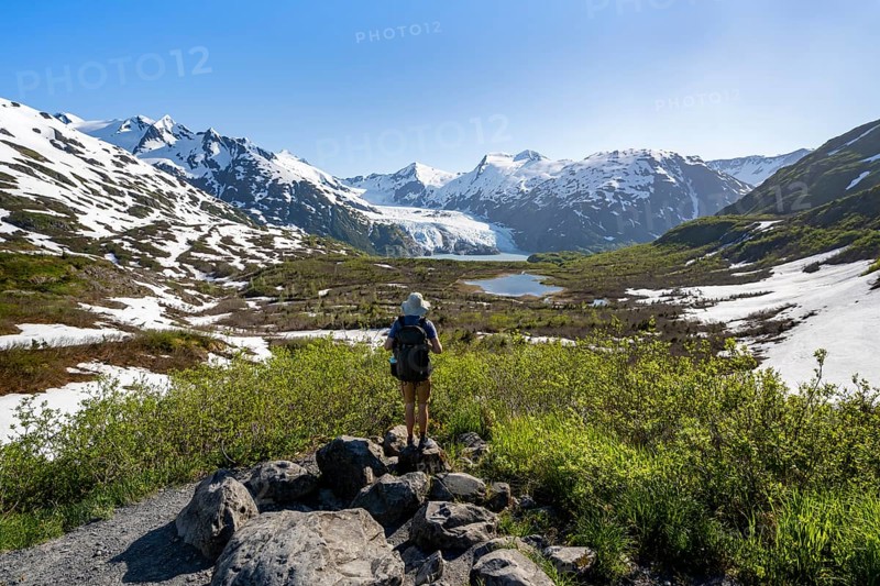 Hiker enjoys views from Portage Pass of Divide Lake, snowy mountain peaks and glaciers Portage Glacier, Portage Pass Trail, near Whittier, Alaska, USA