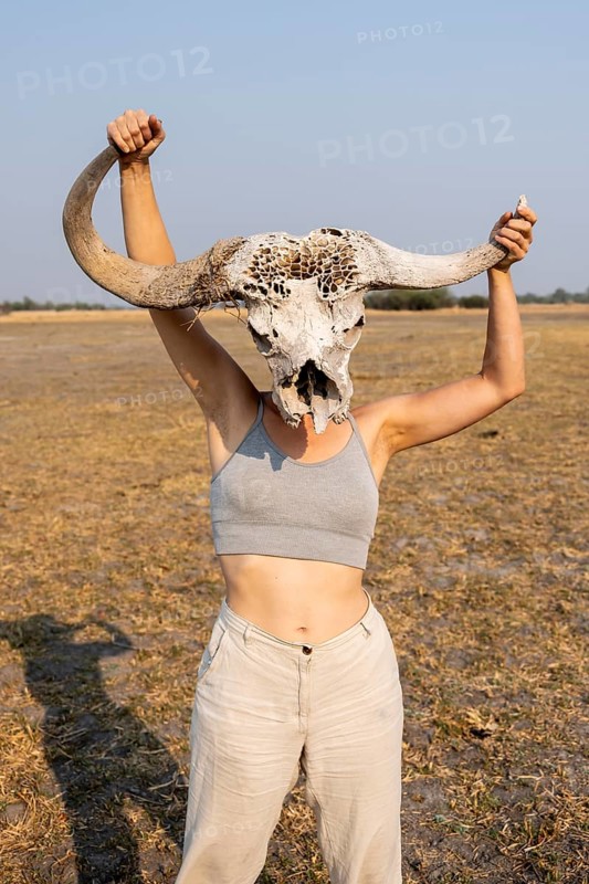 Young woman holding buffalo skull in front of her head, Lustig, Botswana