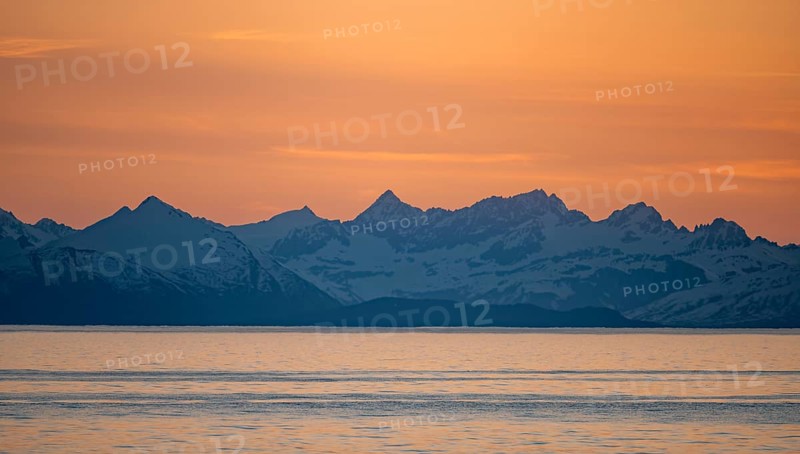 View of Cook Inlet on white mountain peaks of the Aleutian Range, picturesque golden light of the midnight sun, Anchor Point, Anchor River State Recreation Area, Alaska, USA