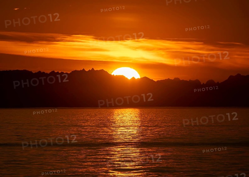 Sun sets behind mountain peaks, view of Cook Inlet at sunset, picturesque golden light of the midnight sun, mountains of the Aleutian Range, Anchor Point, Anchor River State Recreation Area, Alaska, USA