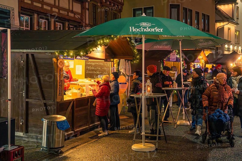 Residents and visitors gather around a food stand with festive lights, Christmas market 2025, Nagold, Black Forest, Calw district, Germany