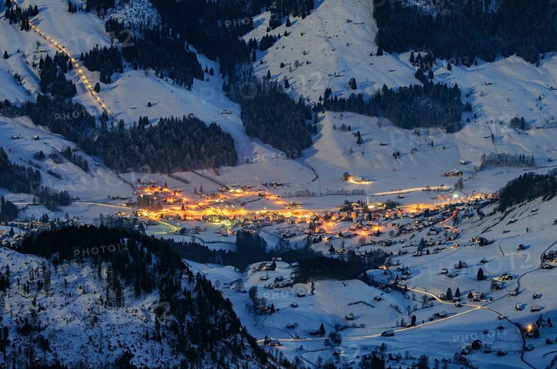 Night shot, long exposure from 2506 meter high SÃ¤ntis into the wintry, snow-covered alpine landscape with the illuminated village of Wildhaus, during a clear full moon night, Canton of Appenzell, Switzerland