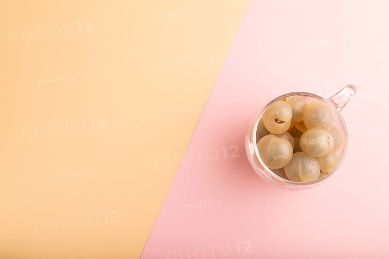 Ripe peeled Longan in glass on pink and orange pastel paper background, top view, flat lay, copy space, minimalism