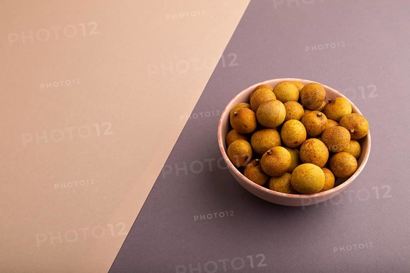 Ripe Longan in ceramic bowl on brown and gray pastel paper background, side view, copy space, minimalism