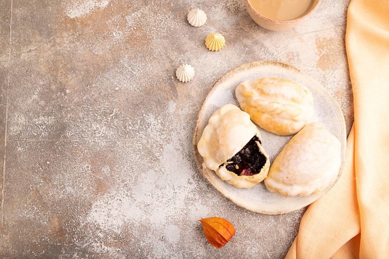 Glazed Pies with blueberry jam on brown concrete background and orange linen textile, cup of coffee, top view, flat lay, copy space