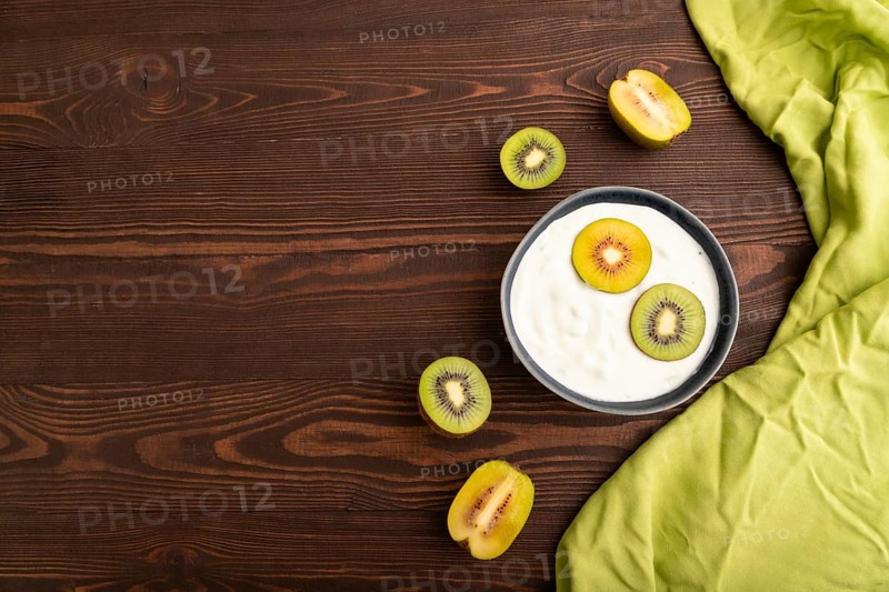 Yogurt, with kiwi in blue bowl on brown wooden background and green linen textile, top view, flat lay, copy space, minimalism