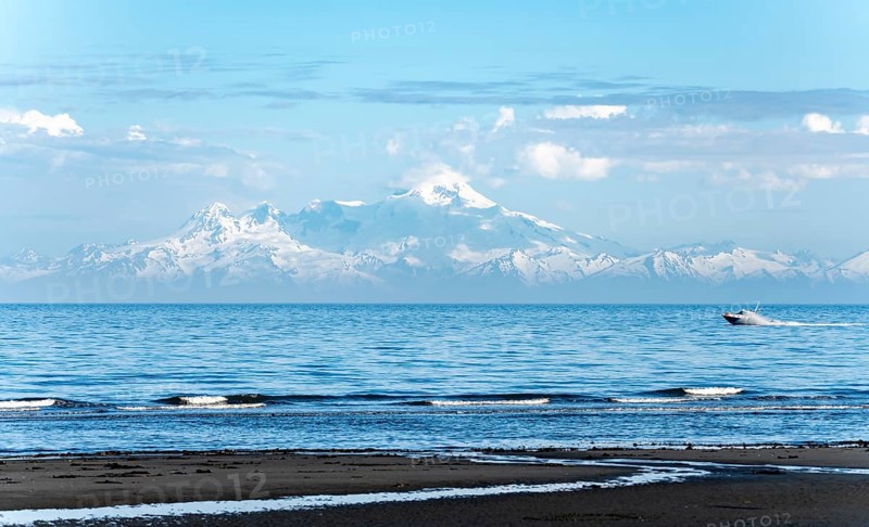 View over Cook Inlet to white mountain peaks of Mount Iliamna, motor boat rides on the ocean, mountains of the Aleutian Range, Anchor Point, Anchor River State Recreation Area, Alaska, USA