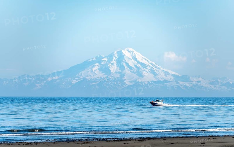 View over Cook Inlet to white mountain peaks of Mount Redoubt, motor boat rides on the ocean, Aleutian Mountains, Anchor Point, Anchor River State Recreation Area, Alaska, USA