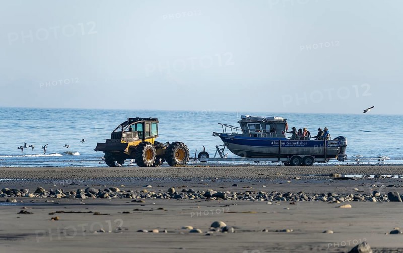 Motor boat on a boat trailer is driven into water by a tractor on a beach, Anchor Point, Alaska, USA