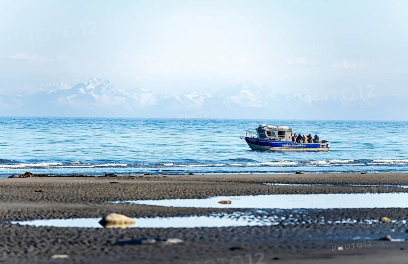View over Cook Inlet to white mountain peaks of the Aleutian Range, motor boat on the ocean, Anchor Point, Anchor River State Recreation Area, Alaska, USA