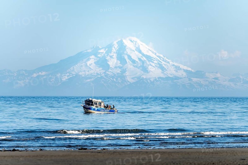 View of Cook Inlet on white mountain peaks of Mount Redoubt, mountains of the Aleutian range, motor boat on the ocean, Anchor Point, Anchor River State Recreation Area, Alaska, USA