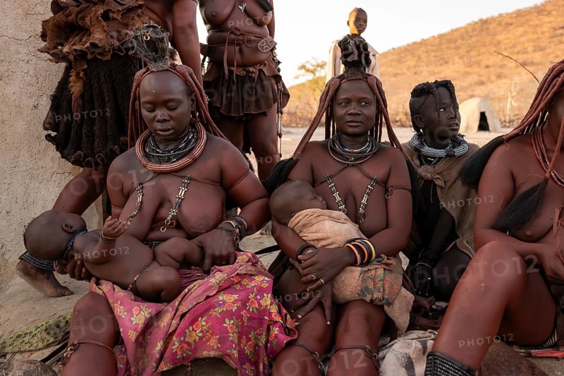 Married Himba woman with their babies in their arms sitting in front of the first woman's hut, in the morning, traditional Himba village, Kaokoveld, Kunene, Namibia