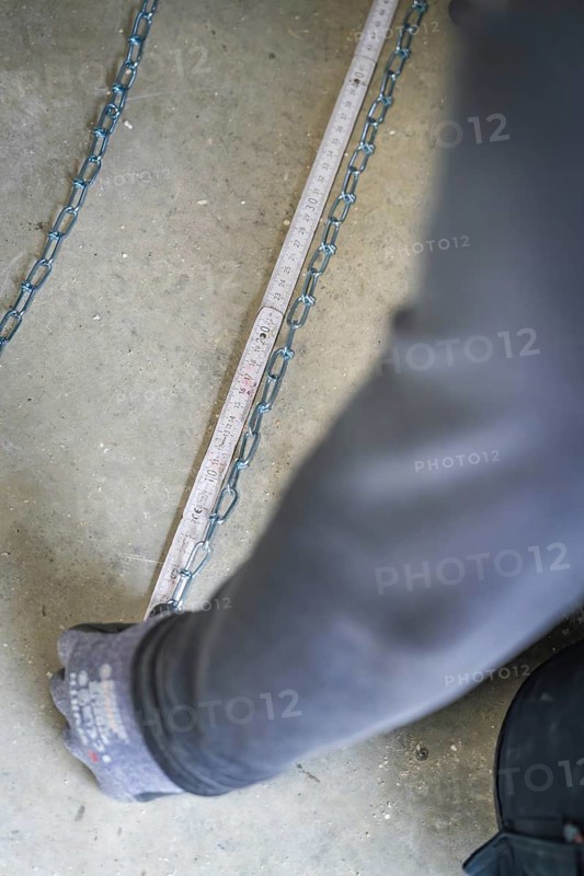 A hand pulls on a chain lying on the ground next to a tape measure, electrician, new building, Germany