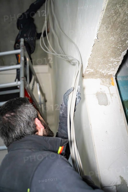 A worker is laying cables along a wall in a renovated room, electrician, new building, Germany