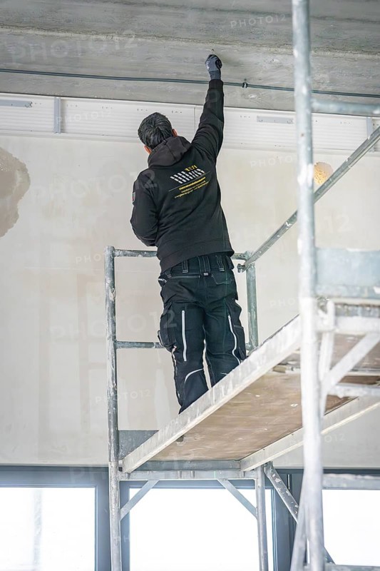 A worker stands on scaffolding and works on the ceiling in a renovated room, electrician, new building, Germany