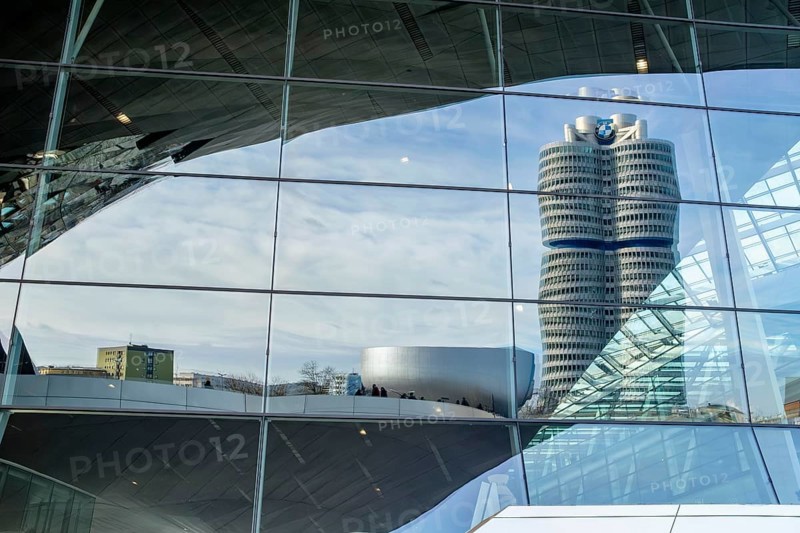 Reflected in the glass faÃ§ade of BMW Welt is the BMW high-rise building, also known as the BMW four-cylinder engine, it serves as the global corporate headquarters, headquarters of the car manufacturer BMW, Munich, Bavaria, Germany