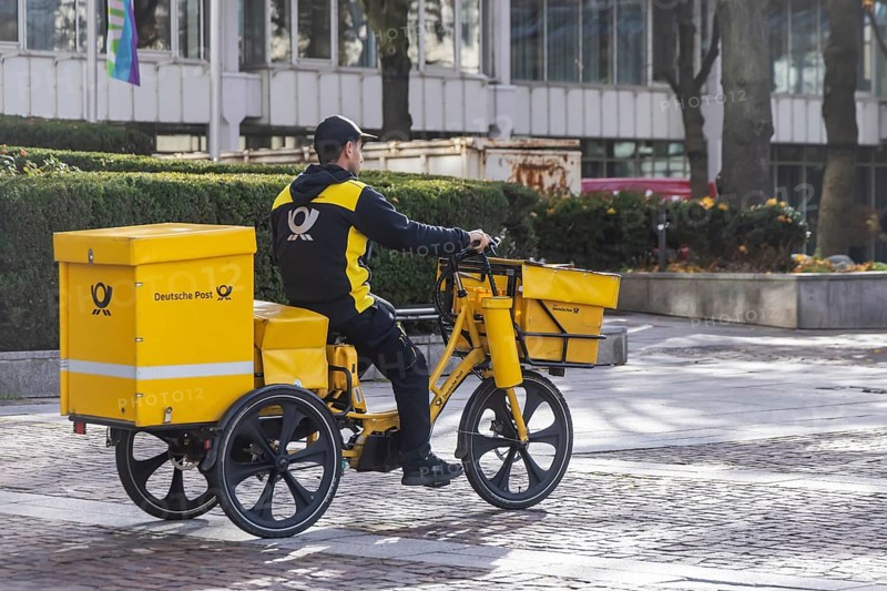 Deutsche Post mailmen on a bicycle through the city. Stuttgart, Baden-WÃ¼rttemberg, Germany