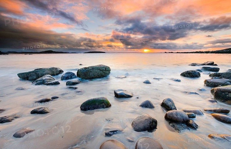 Orange cloudy sky at sunset on a sandy beach with round stones near Achiltibuie on the west coast of Scotland