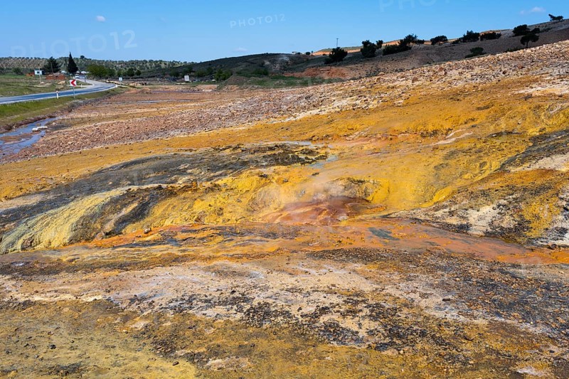 A colorful natural landscape with yellow and orange rocks next to a road under a blue sky, geothermal area, rainbow rocks Tuzla, AyvacÄ±k, Ayvacik, Ã‡anakkale, Canakkale, Turkey