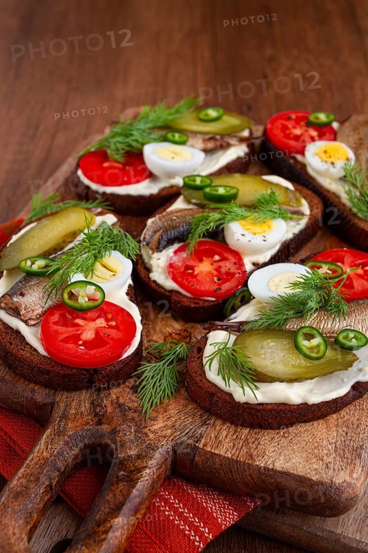 Sandwiches on rye bread with sprats, quail eggs, fresh tomatoes and pickled cucumber, on a wooden board, appetizer, breakfast