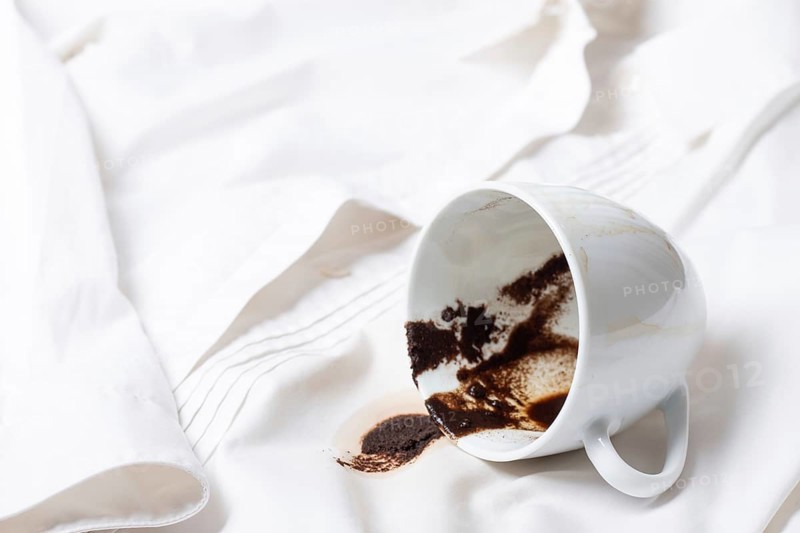 A white cup with the remains of coffee, spilled, lies on a white shirt, there are no people, a soft focus