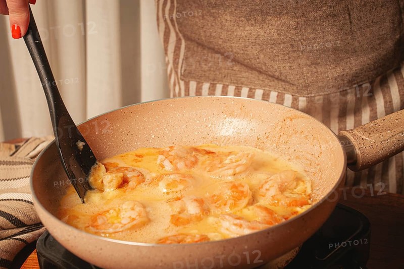 In a cozy kitchen, a person is stirring shrimp in a creamy sauce on the stove. The scene captures the joy of cooking, with warm colors and inviting textures
