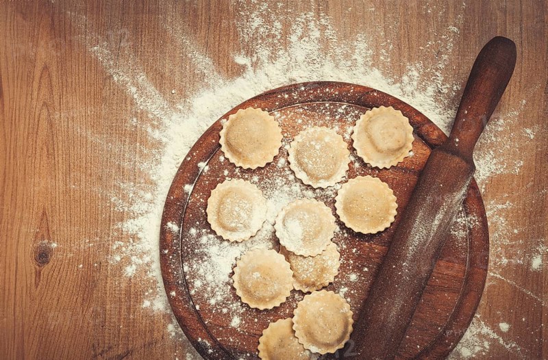 Fresh raw, uncooked ravioli, on a cutting board, with a rolling pin for dough, wooden background, no people