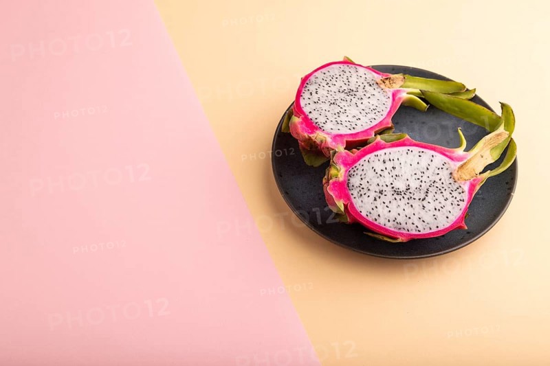 Ripe Pitaya on blue plate on pink and orange pastel paper background, side view, copy space, minimalism