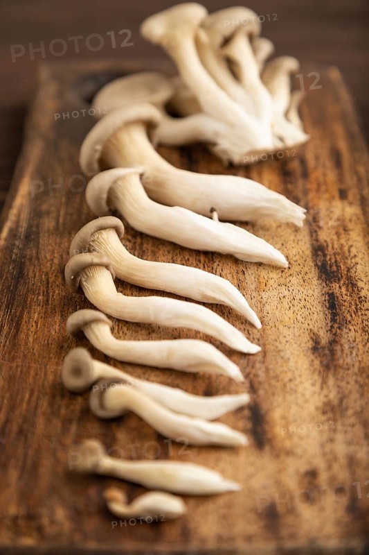 Raw Oyster mushroom, Pleurotus ostreatus on cutting board on brown wooden background. Side view, minimalism, selective focus