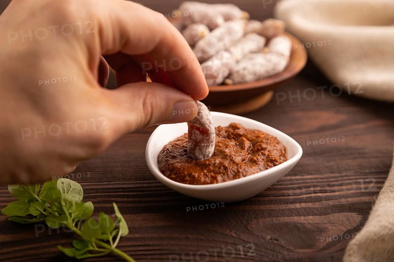 Small smoked Chicken sausages in wooden bowl with hand on brown wooden background and linen textile. side view, close up, selective focus