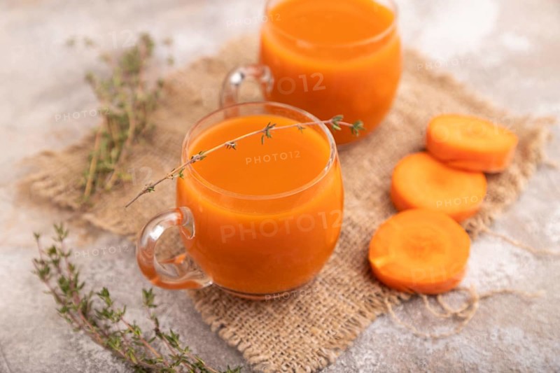 Two glasses with carrot juice, on brown concrete background and linen textile. Diet, healthy eating concept. side view, close up, minimalism, selective focus