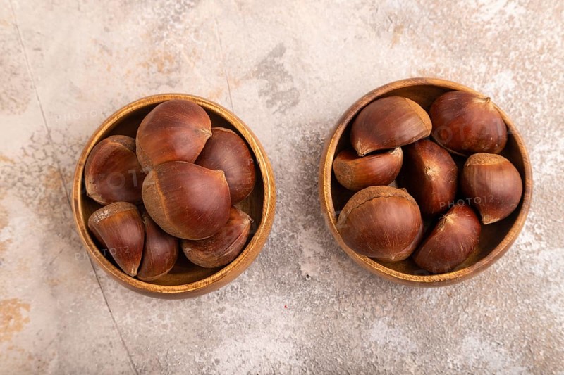 Wooden bowl with raw edible Ð¡hestnuts on brown concrete background, top view, flat lay, close up, minimalism