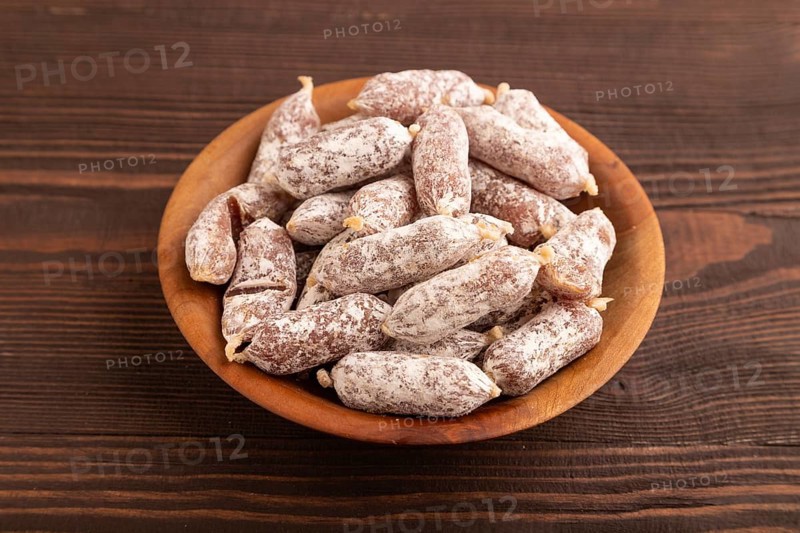 Small smoked Chicken sausages in wooden bowl on brown wooden background. side view, close up