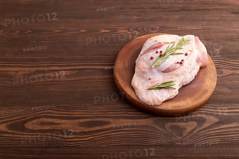 Raw Turkey Thigh with spices and rosemary on cutting board on brown wooden background. side view, copy space