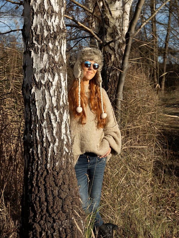 Slender pretty woman with fur hat and sweater, red hair and warm winter colors between birch forest and reeds