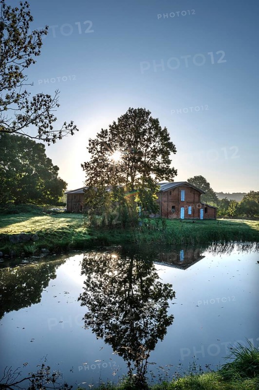 Manor with historic stable and pond, from 1923, in backlight with sun star, Gut Othenstorf, Mecklenburg-Western Pomerania, Germany