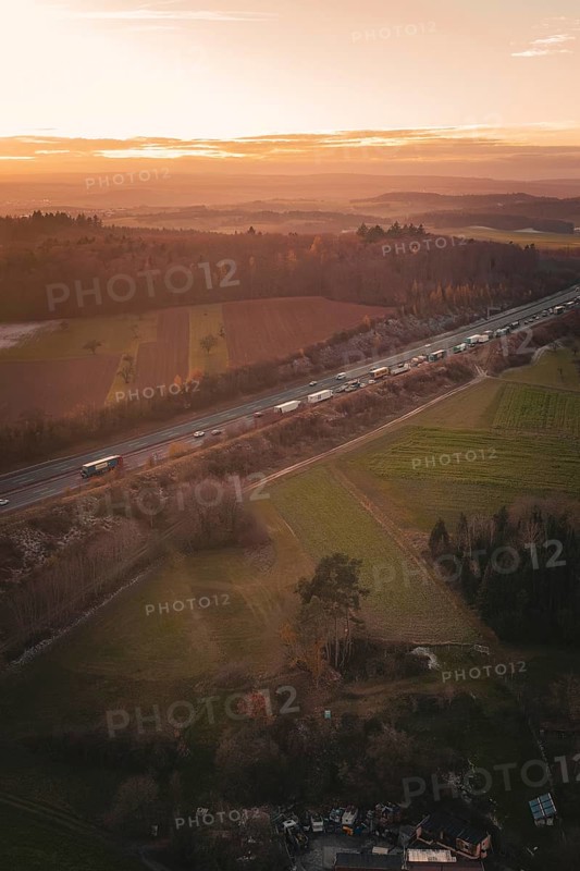 Aerial view of a motorway surrounded by fields and forests as the orange sunset colors the sky, A8 motorway, Germany