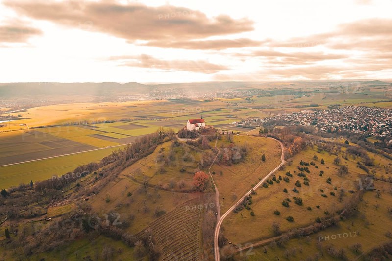 A hill with a church and a wide view over fields and a village under a cloudy sky, Wurmlinger Chapel, Rottenburg am Neckar, Germany