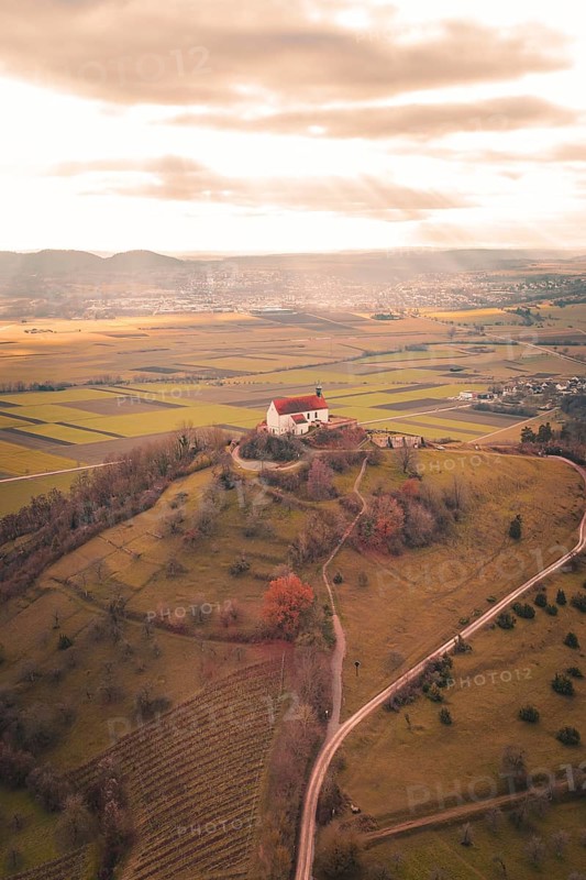 A red church roof on a hill with a view of vast fields under a cloud cover, Wurmlinger Chapel, Rottenburg am Neckar, Germany