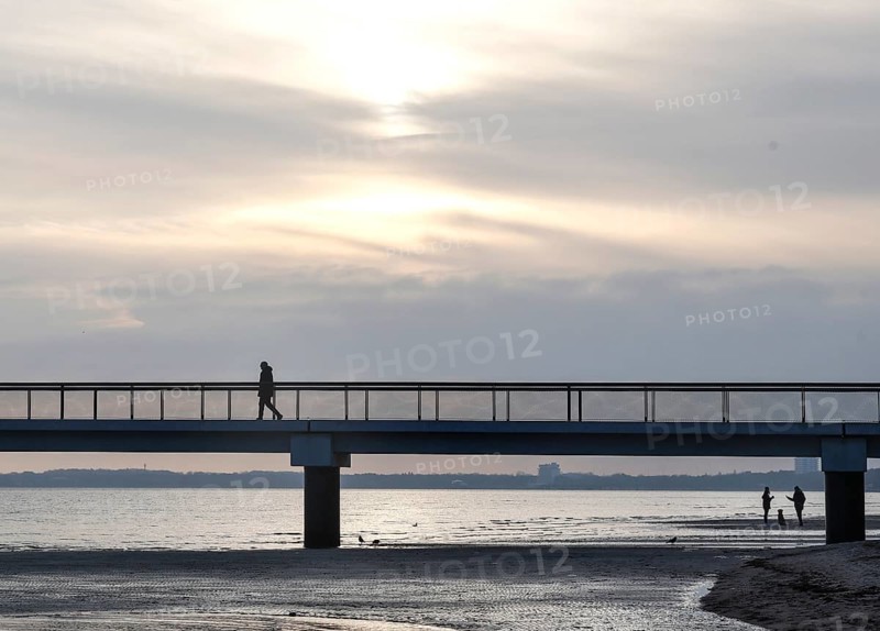 Silhouettes of people on and under a pier, low tide, wave and ripple patterns in wet sand, sunrise, Scharbeutz, 29.11.2025, Scharbeutz, Schleswig-Holstein, Germany
