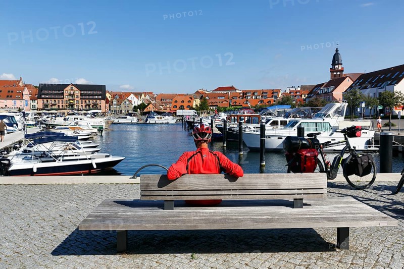 Cyclist with helmet, sitting on a wooden bench, e-bike with luggage bags, bike tour, boats in the city harbor, Waren an der MÃ¼ritz, Mecklenburg Lake District, Mecklenburg-Western Pomerania, Germany