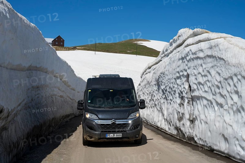 A van drives through thick snow walls on a mountain road under a blue sky, motorhome, camper on a road in a snowwall on the Goderdzi Pass, Ajara region, Adjara, autonomous republic, Georgia