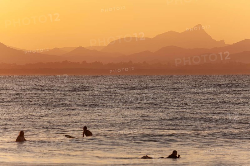 Red sunset on Wategos Beach with surfers in the ocean. Mt. Warning, Wollumbin in the background of the surfing scene. Byron Bay, New South Wales, Australia