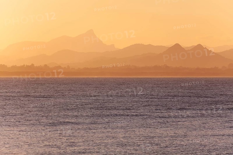 View of the ocean and Byron Bay hinterland at sunset. Mt. Warning, Wollumbin National Park over the bay in the evening light. New South Wales, Australia