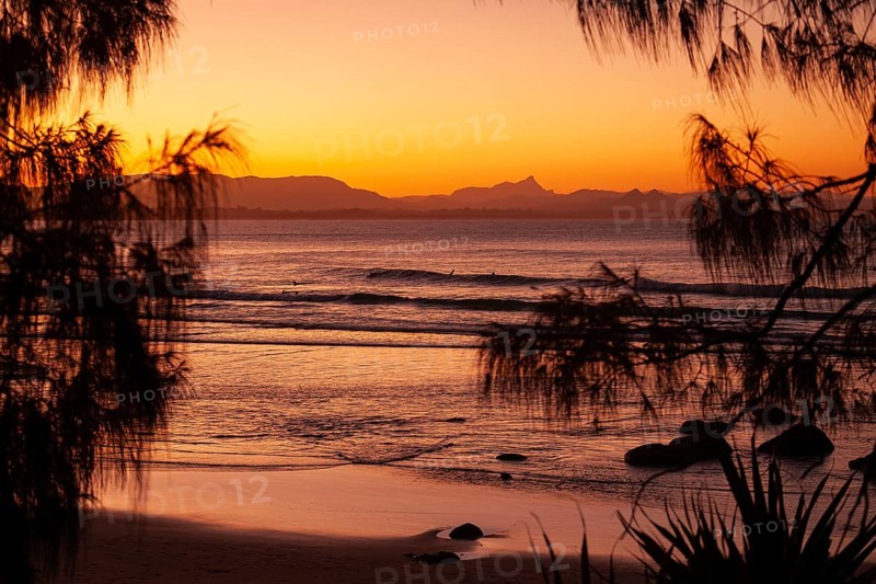 View of the ocean and Wategos Beach on the promenade at sunset. Mt- Warning, Wollumbin in the background of the red sunset on the beach