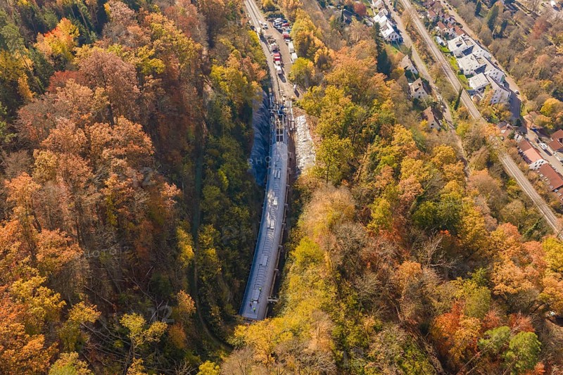 Bird's-eye view of a tunnel construction project integrated into an urban and autumnal forest landscape, Hermann Hesse Railway Bat Tunnel construction site, Calw, Black Forest, Germany