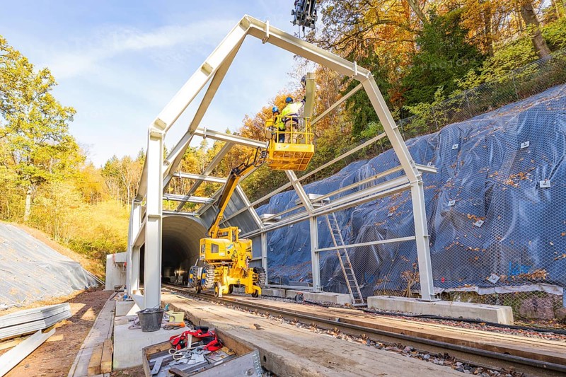 Construction work on a tunnel opening with cranes and workers against an autumn backdrop, Hermann Hesse Railway bat tunnel construction site, Calw, Black Forest, Germany