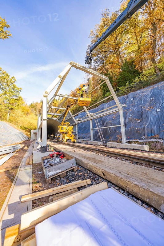 Crane lifts construction material for a tunnel surrounded by autumnal forest and blue skies, Hermann Hesse Railway Bat Tunnel construction site, Calw, Black Forest, Germany
